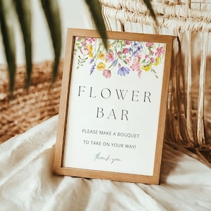May include: A wooden framed sign with a floral design and the text "FLOWER BAR" with the words "Please make a bouquet to take on your way! Thank you." printed below.