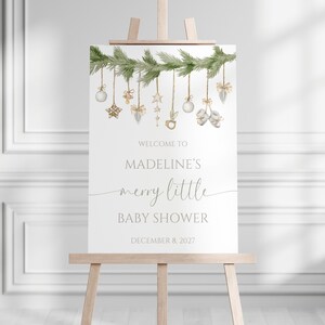 Merry Little Baby Shower Welcome Sign includes christmas greenery, baby shower items, and ornaments. Photo shows 18x24" sign on an easel.