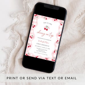 May include: A smartphone displaying a digital invitation with a pink and white gingham background, red cherry illustrations, and text that reads: SHE IS THE cherry on top, PLEASE JOIN US IN CELEBRATING, Kaeleigh Mae's, FIRST BIRTHDAY, SATURDAY, JUNE 27 | 2PM.