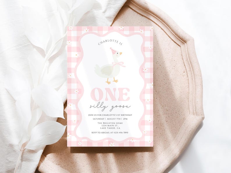 May include: A pink and white invitation card with a gingham pattern and a whimsical illustration of a goose wearing a party hat. The text reads "ONE silly goose" and includes event details. The card is on a light-colored surface.