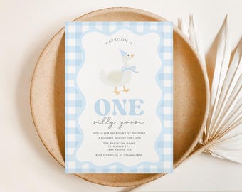 May include: A light blue and white gingham patterned invitation card with the text "ONE silly goose" and event details. The card features a cartoon goose wearing a party hat and bow. The invitation is on a beige plate.