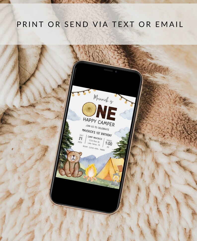 May include: A digital invitation for a first birthday party with a woodland theme. The invitation features a cartoon bear, a campfire, a tent, and a wooden sign that says "Maverick is One Happy Camper". The invitation includes the date, time, and location of the party.