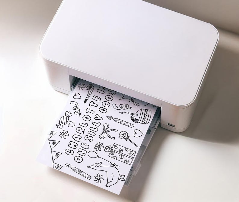 May include: A white printer is printing a black and white coloring page. The page features the text "CHARLOTTE ONE SILLY GOOSE" along with various illustrations of a birthday theme, including a cake, candles, and a dog with a balloon.