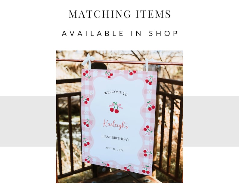 May include: A rectangular sign with a pink and white gingham border featuring red cherry illustrations. The text reads: MATCHING ITEMS AVAILABLE IN SHOP, WELCOME TO, Kaeleigh's, FIRST BIRTHDAY, JULY 21, 2029. The sign is suspended by white ribbons.