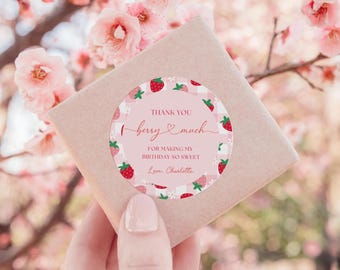 Può includere: Un adesivo rotondo con sfondo a quadretti rosa chiaro e bianco con illustrazioni di fragole rosse. Il testo recita: THANK YOU berry much FOR MAKING MY BIRTHDAY SO SWEET Love, Charlotte. L'adesivo è attaccato a un pacchetto di carta marrone.