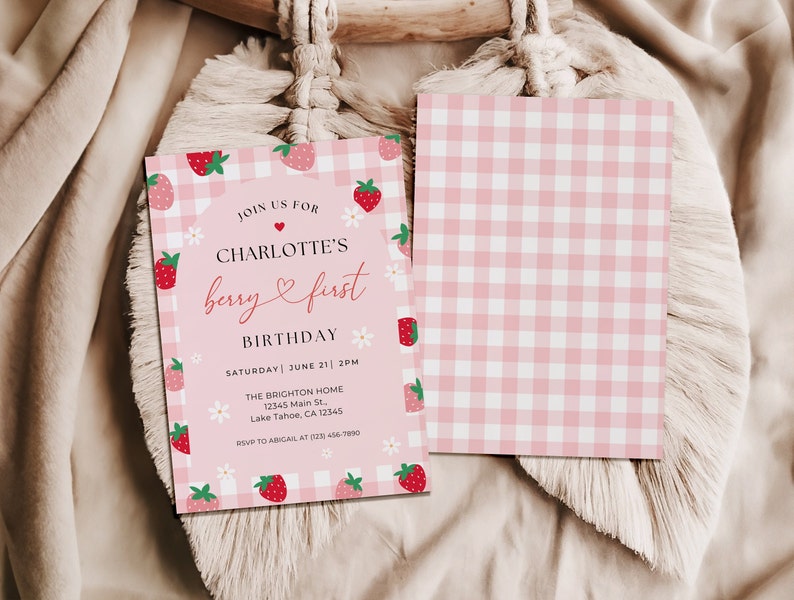 Berry first birthday invitation shows the front and bottom of the invite. The back of the invite has pink and whitegingham print. Photo shows the front and back of the invite laying flat.