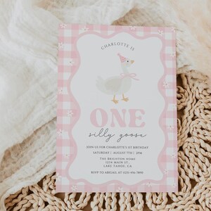 May include: A pink and white invitation card with a gingham border and a whimsical illustration of a goose wearing a party hat. The text reads "ONE silly goose" and includes event details. The card is on a neutral background.