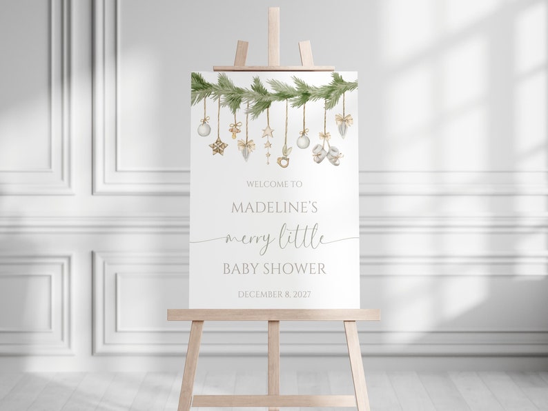 Merry Little Baby Shower Welcome Sign includes christmas greenery, baby shower items, and ornaments. Photo shows 18x24" sign on an easel.