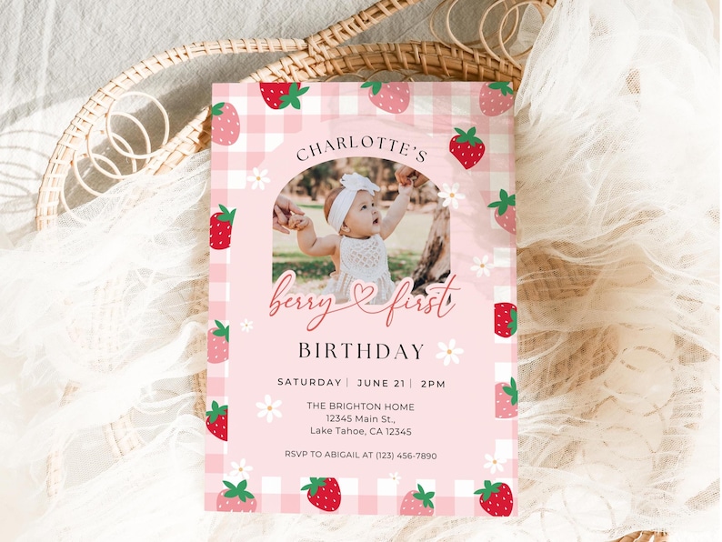 May include: Pink and white gingham patterned invitation with a photo of a baby girl in a white dress. The invitation says "Charlotte's Berry First Birthday" and includes the date, time, and location of the party. RSVP information is also included.