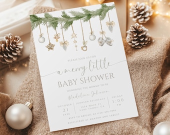 May include: A white baby shower invitation featuring a green pine branch garland adorned with ornaments and a handwritten message that reads "a merry little baby shower". The invitation includes the date, time, location, and RSVP details for the event.