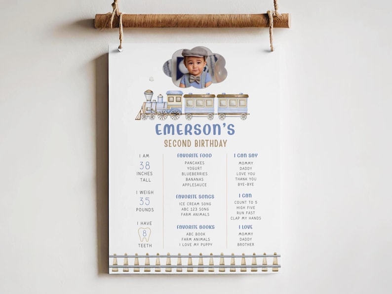 Train 2nd Birthday Milestone Sign is shown printed as an 18x24" sign hanging from a decorative string and wooden display against a wall. The chugga chugga two two sign includes a place for a photo on the top in the shape of a cloud, a blue and beige watercolor train underneath and editable text that reads, "Emerson's second birthday." Editable text for milestones include weight, height, favorite food, favorite songs, favorite books, what he can say, etc."