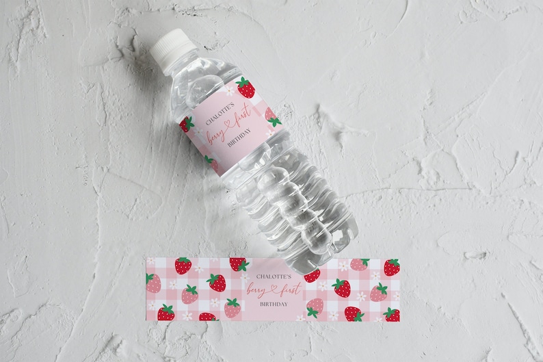 Berry First Birthday Water Bottle Labels with pink gingham pattern, pink and red strawberries. and white daisies. Place for name above "berry first birthday" quote. Photo shows water bottle laying flat with label wrapped aroud it.