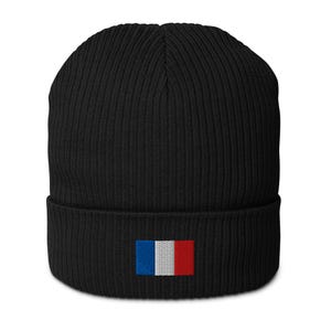 May include: A black beanie with a ribbed knit texture. The beanie features a small embroidered French flag on the front, with blue, white, and red vertical stripes. This winter hat is a stylish accessory.