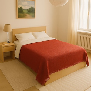 Może przedstawiać: Sypialnia z drewnianym stelażem łóżka i czerwoną kołdrą. Łóżko ma dwie białe poduszki i białą pościel. Obok łóżka stoi mały drewniany stolik nocny z lampą. Pokój ma biały sufit i białe ściany. W tle znajduje się okno z białymi zasłonami.