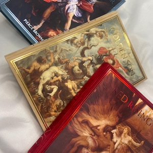 May include: Three hardcover books with colorful artwork. The top book is blue with a painting of a man in action. The middle book is gold with a painting of a battle scene. The bottom book is red with a painting of figures.