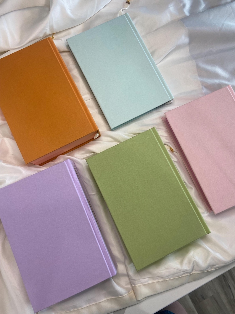 Pode incluir: Cinco cadernos de capa dura com diferentes cores de capa: laranja, azul claro, rosa, verde e lavanda.