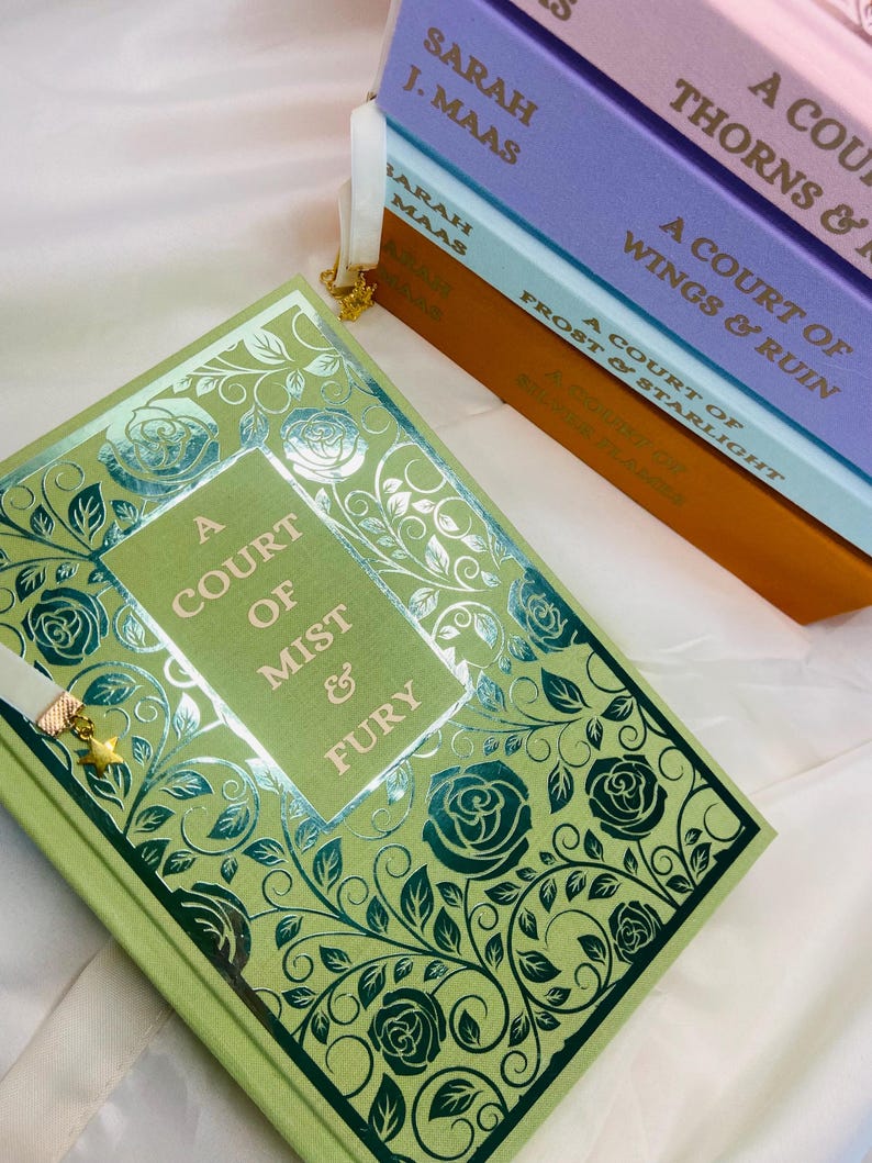 Pode incluir: Um livro de capa dura verde com um design de rosas e videiras em folha de prata. O t&iacute;tulo &eacute; "A Court of Mist & Fury" de Sarah J. Maas.