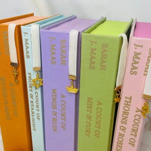 Pode incluir: Um conjunto de seis livros de capa dura com lombadas de cores combinando e marcadores de fita branca. Os livros s&atilde;o intitulados "A Court of Thorns & Roses", "A Court of Mist & Fury", "A Court of Wings & Ruin", "A Court of Frost & Starlight", "A Court of Silver Flames", e "A Court of ...".