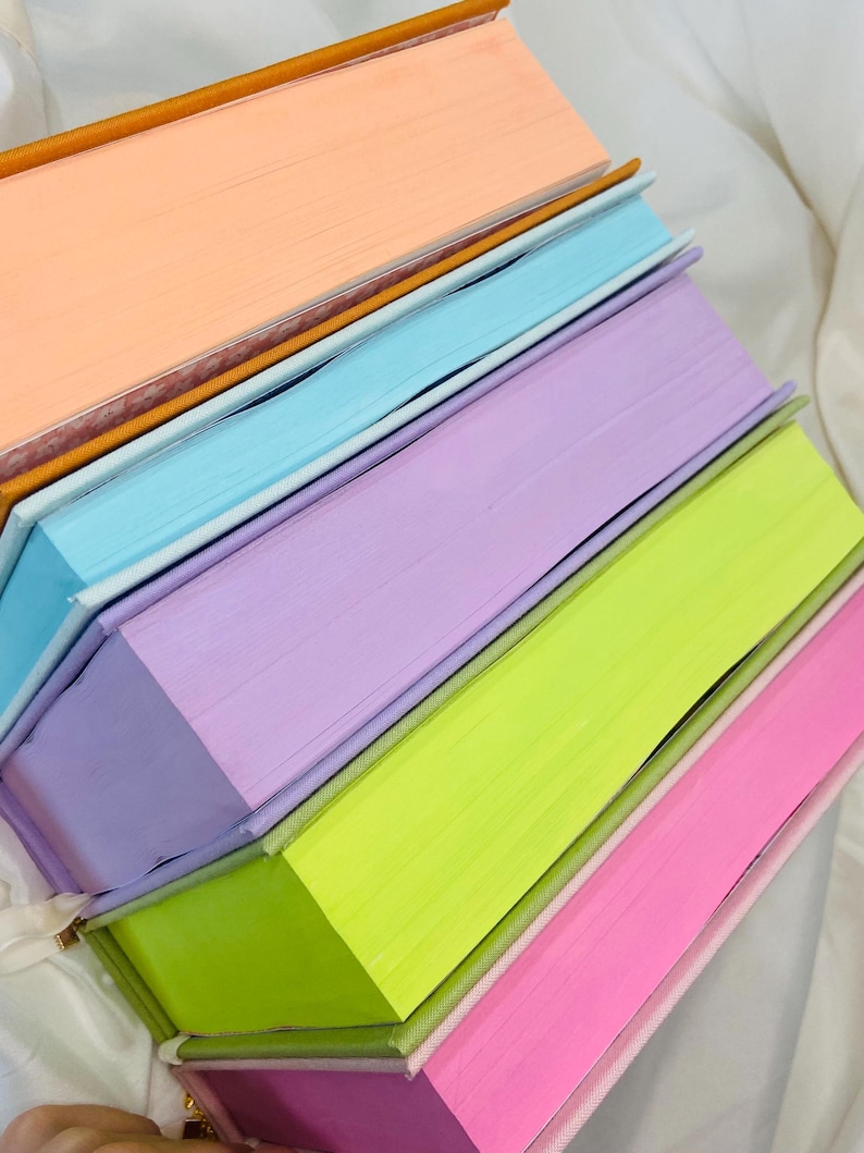 Pode incluir: Uma pilha de cinco livros com capas coloridas. As capas s&atilde;o p&ecirc;ssego, azul claro, lavanda, verde lim&atilde;o e rosa.