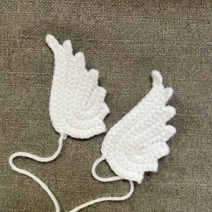 May include: Two white crocheted angel wings with a white yarn string attached to each wing.