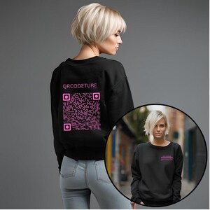 Könnte beinhalten: Schwarzes Sweatshirt mit einem rosa QR-Code und dem Text "QR CODETURE" auf der Rückseite. Das Sweatshirt wird an einem Model mit kurzen blonden Haaren gezeigt.