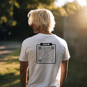 Könnte beinhalten: Ein weißes T-Shirt mit einem schwarz-weißen QR-Code auf der Rückseite. Der Text "SCAN ME" befindet sich über dem QR-Code.