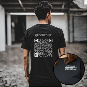 Könnte beinhalten: Schwarzes T-Shirt mit einem weißen QR-Code und dem Text "QRcodeture" auf der Rückseite. Der Text "INSTAGRAM: QRcodeture" ist unten auf dem Shirt sichtbar.