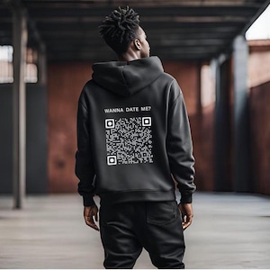 Könnte beinhalten: Schwarzer Hoodie mit einem weißen QR-Code und dem Text "Wanna Date Me?" auf der Rückseite.