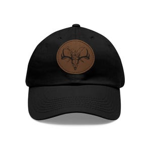 May include: Black baseball cap with a curved brim. A brown leather patch on the front features a graphic of a deer skull with crossed swords. The cap is made of a durable fabric and has an adjustable strap.