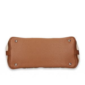 Pu&ograve; includere: Vista dal basso di una borsa in pelle marrone con superficie strutturata. La borsa ha quattro piedini in metallo argentato e pannelli laterali in tela color crema. Gli angoli sono arrotondati e le cuciture sono visibili.
