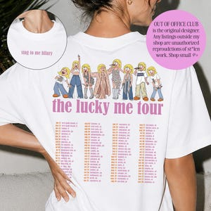 May include: A white t-shirt featuring a graphic of eight cartoon figures in various outfits above the pink text 'the lucky me tour' and a list of tour dates. A circular inset shows the collar area with the text 'sing to me hilary'.