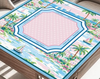 May include: A square game table cover with a tropical beach scene. The cover features palm trees, sailboats, and a pink and blue central design with text that reads "Walls Left" and "Play Right". The cover is on a wooden table.