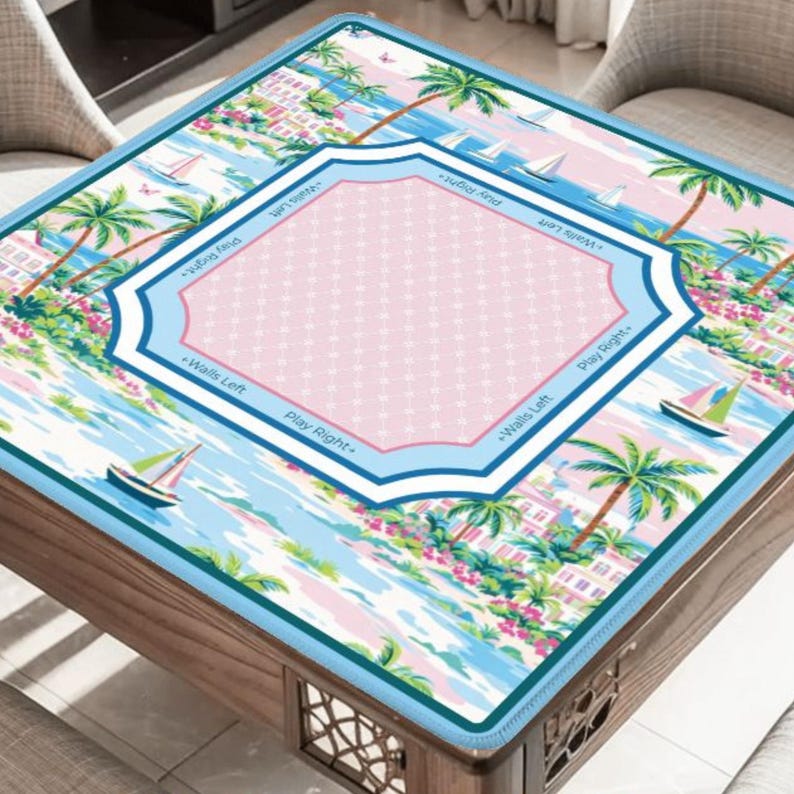 May include: A square game table cover with a tropical beach scene. The cover features palm trees, sailboats, and a pink and blue central design with text that reads "Walls Left" and "Play Right". The cover is on a wooden table.