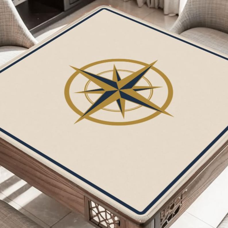 May include: A square table with a cream-colored top featuring a compass rose design in gold and navy blue. The table has a dark blue border and a wooden base. The table is surrounded by two chairs.