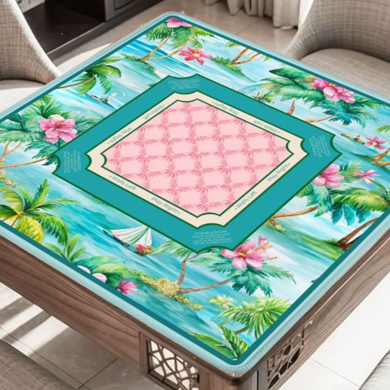 May include: A square game table cover featuring a tropical design with palm trees, pink flowers, and a sailboat. The center has a pink grid pattern within a teal frame. The edges are teal with text.