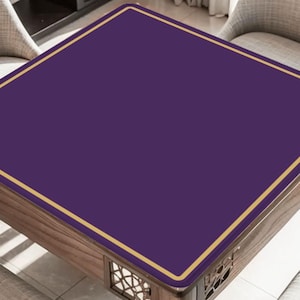 May include: A square table with a deep purple surface and a thin gold border. The table has a wooden frame with decorative cutouts on the sides. The table is surrounded by two chairs.