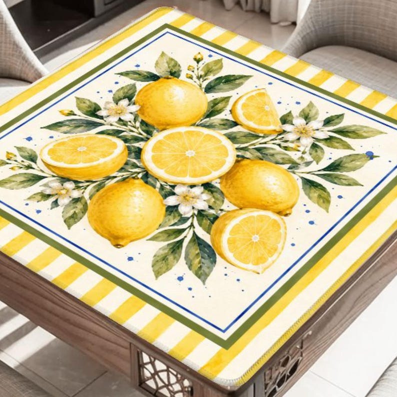 May include: A square table cover featuring a vibrant lemon design. The cover showcases whole and sliced lemons, white flowers, and green leaves. The border has a striped yellow and white pattern with a green and blue trim.
