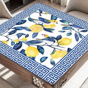 May include: A square table cover featuring a white background with a watercolor design of yellow lemons, blue birds, and green leaves. The border is a blue and white geometric pattern. The table is made of wood.