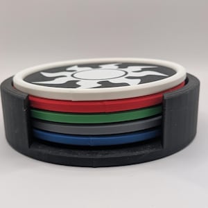 May include: A set of four black, white, red, green, blue and gray coasters with a black and white sun design on the top coaster.