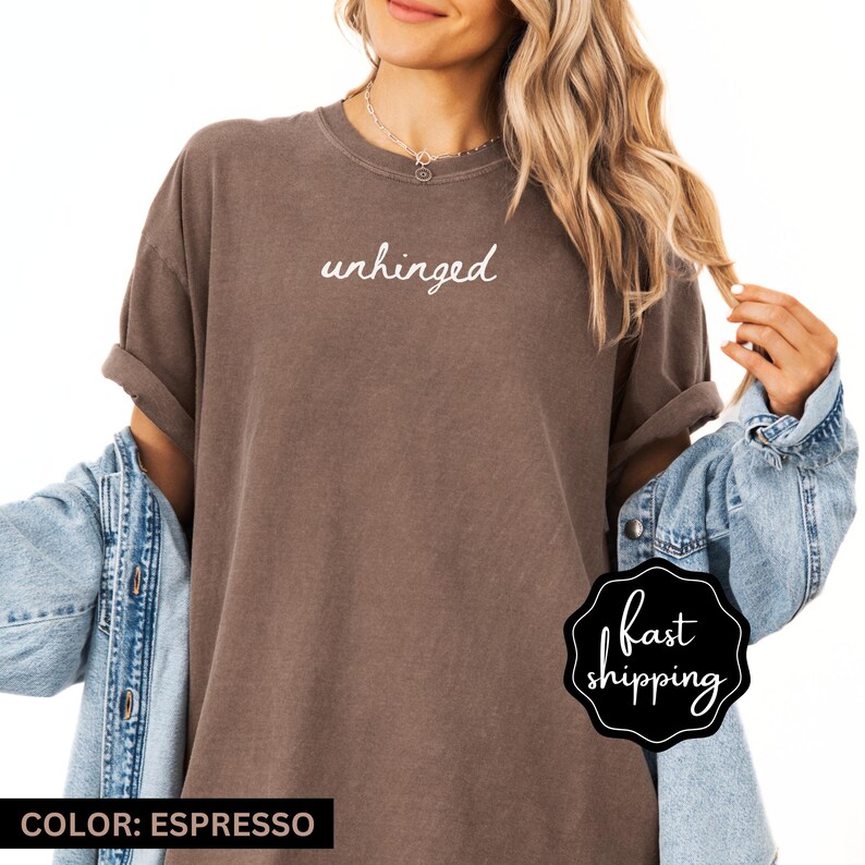 May include: A brown oversized t-shirt with the word "unhinged" printed in white on the front. The shirt is being modeled by a person wearing a denim jacket.