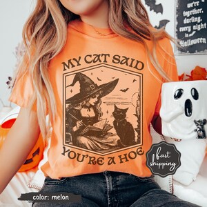 May include: Melon-colored t-shirt with a witch and cat graphic. The graphic includes the text "MY CAT SAID YOU'RE A HOE". The shirt is a Halloween-themed design.