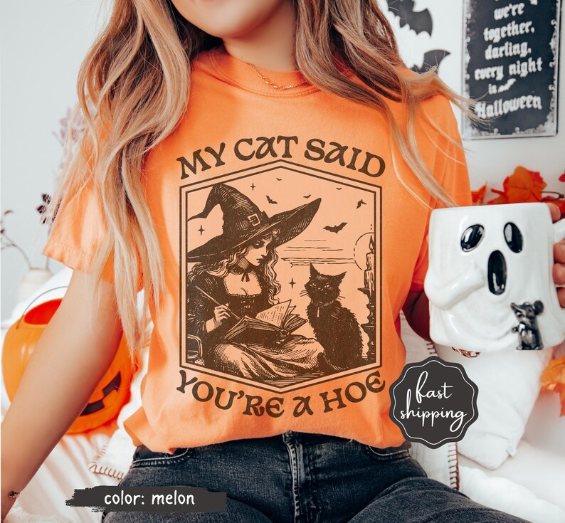 May include: Melon-colored t-shirt with a witch and cat graphic. The graphic includes the text "MY CAT SAID YOU'RE A HOE". The shirt is a Halloween-themed design.