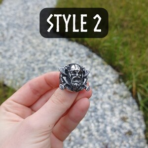 Pu&ograve; includere: Un anello d'argento con un design a testa di guerriero vichingo. L'anello raffigura un guerriero con un elmo cornuto, barba e spade incrociate. Il testo "STYLE 2" &egrave; visibile sullo sfondo.
