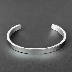 Puede incluir: Un brazalete de plata con un acabado liso y pulido.