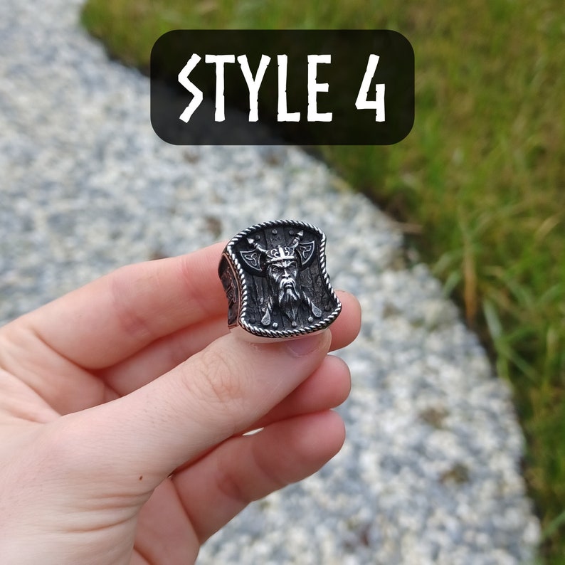 Pu&ograve; includere: Un anello d'argento con un design a scudo che presenta la testa di un guerriero vichingo. Lo scudo &egrave; dettagliato con un bordo di corda e due asce. L'anello &egrave; etichettato "STYLE 4".
