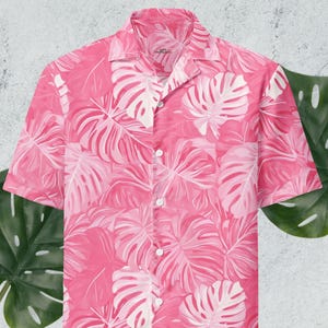 May include: A pink short-sleeved button-up shirt with a white tropical leaf pattern.