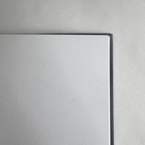 May include: A blank white notebook with a black spine. The notebook is closed and lying flat on a light gray surface.