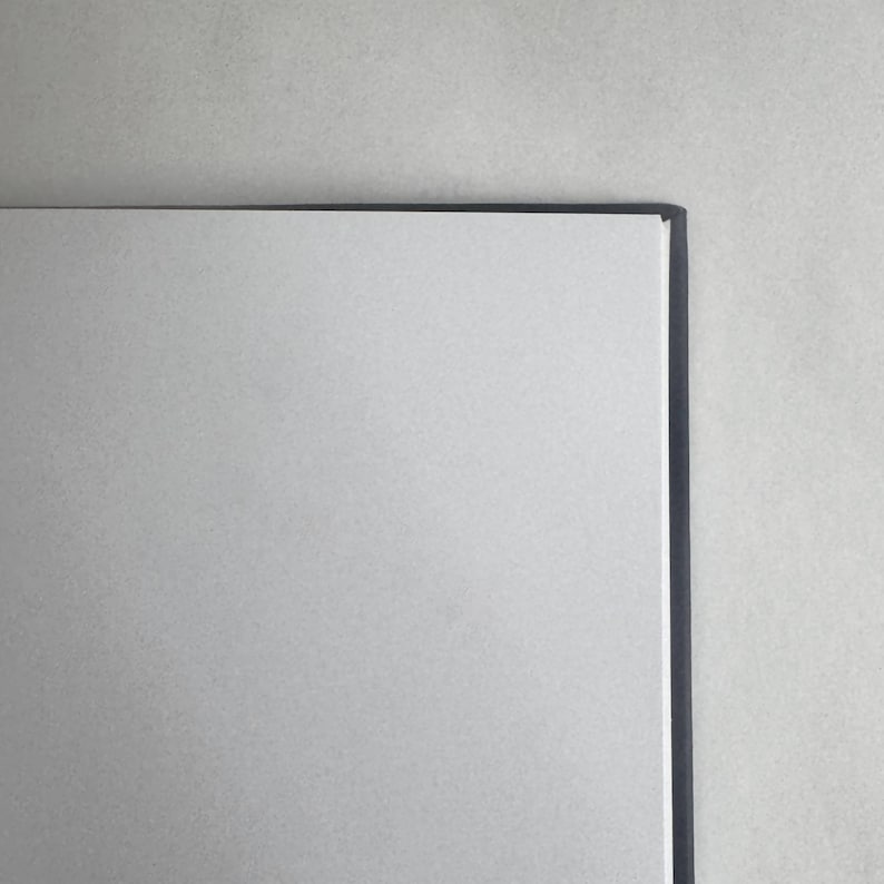 May include: A blank white notebook with a black spine. The notebook is closed and lying flat on a light gray surface.