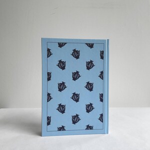 May include: A light blue book cover with a repeating pattern of black and white illustrations of vases.