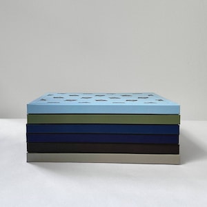 May include: A stack of five notebooks with different colored covers. The top notebook has a light blue cover with a pattern of small, dark blue shapes. The other notebooks have green, dark blue, brown, and light gray covers.